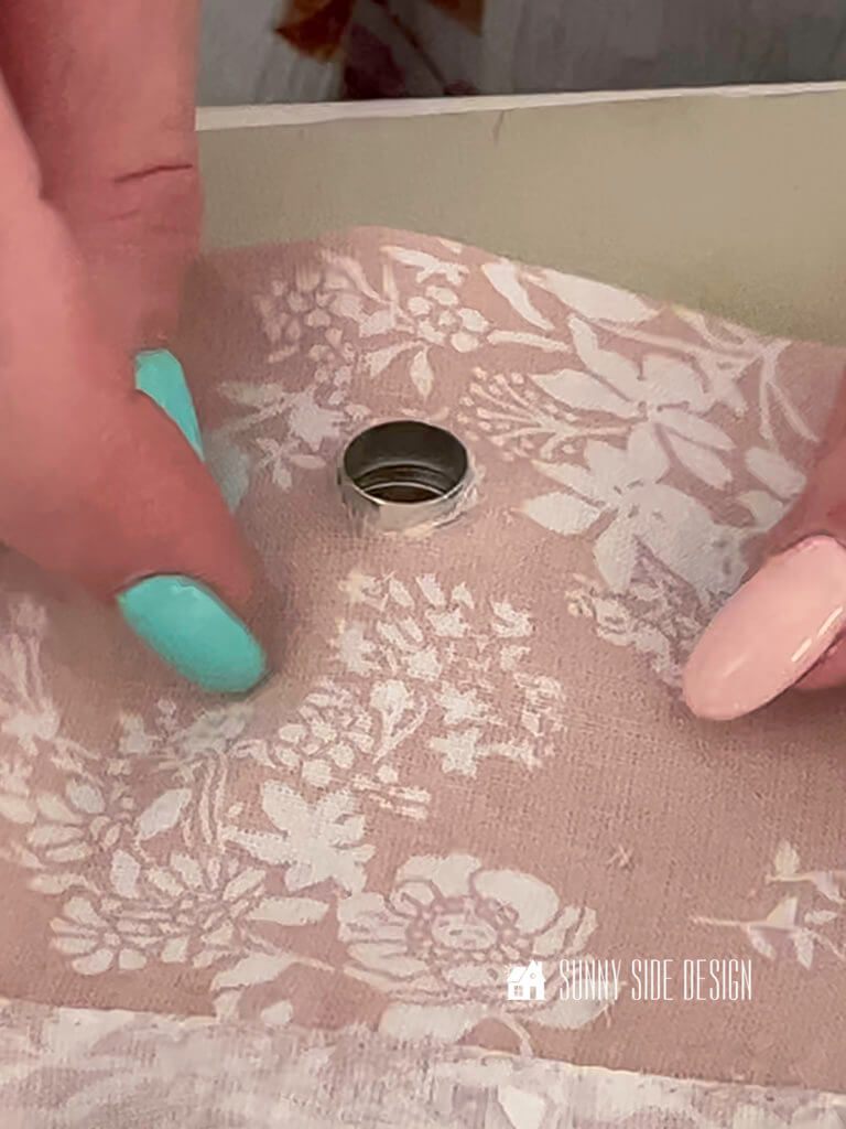 Woman's hand holding flat sheet, pressing grommet through hole to make a shower curtain.