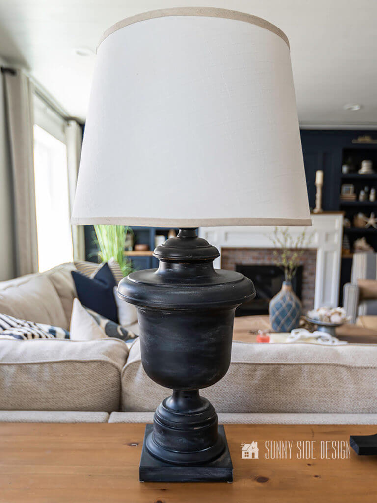 Aged black lamp makeover setting on natural wood sofa table with navy blue entertainment center in the background.