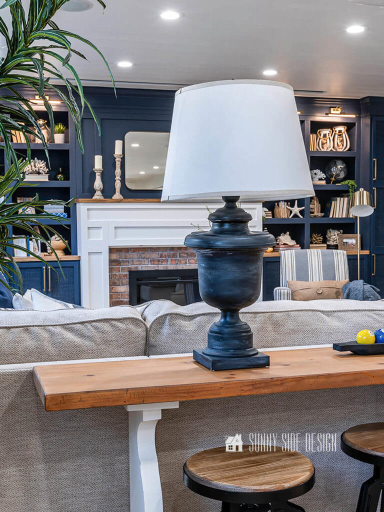 Aged black lamp makeover setting on natural wood sofa table with navy blue entertainment center in the background.