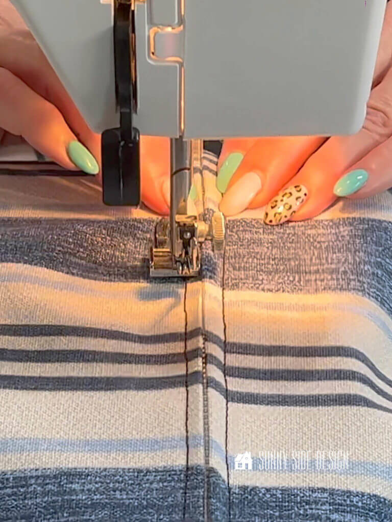 Make a box cushion, Woman's hand feeding the fabric with the zipper through the sewing machine.