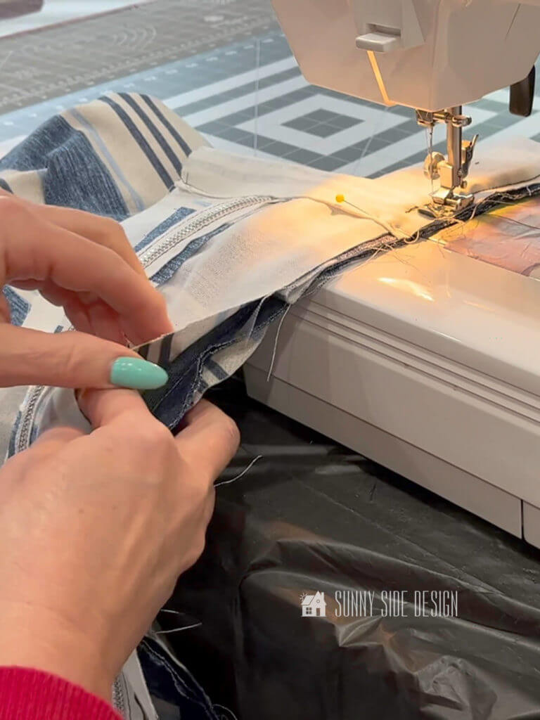 Make a simple box cushion, Woman's hands holding thr blue and white striped fabric at the sewing machine stitching the zipper section of the box cushion to the piping.