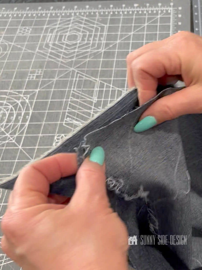 Woman's hands holding the bias cut denim aligning the white pencil lines when making the piping for a box cushion.
