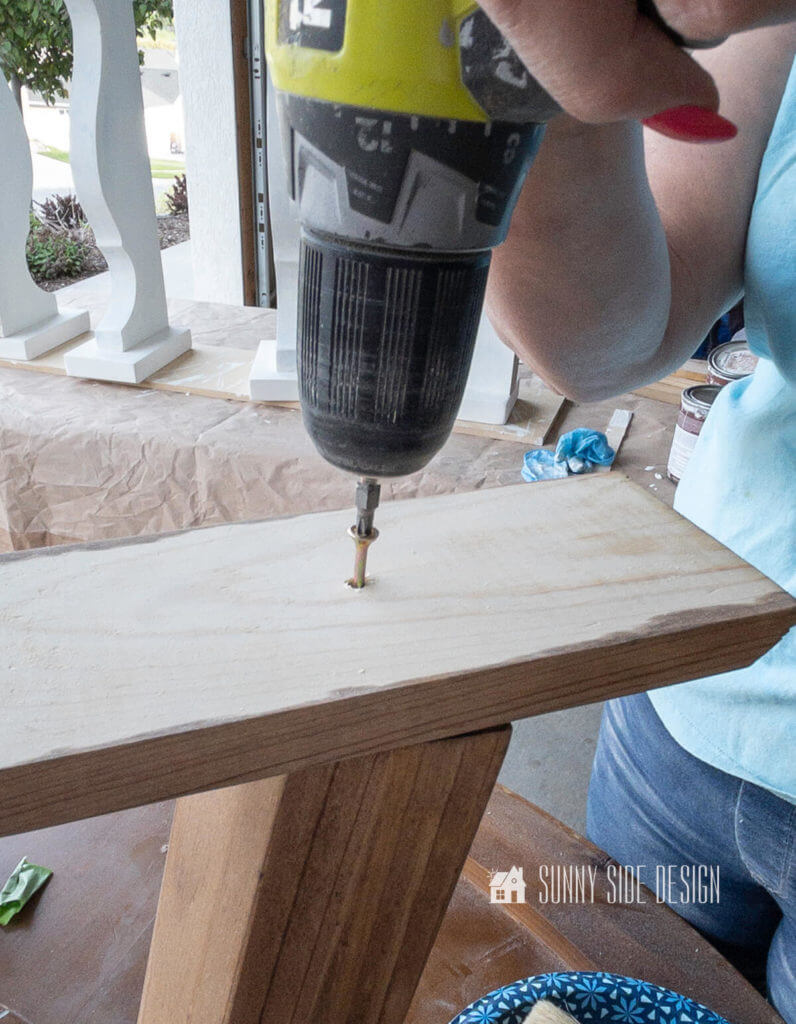 Woman holding drill inserting a screw in the leg base of the DIY round coffee table.
