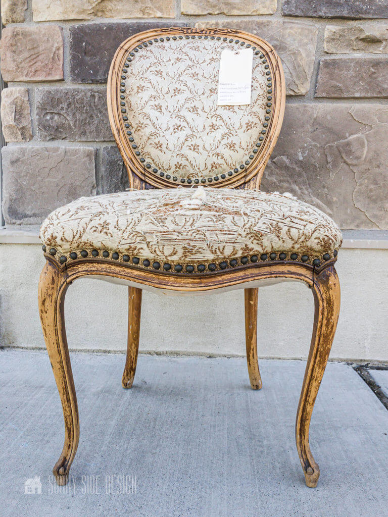 Vintage and worn French styled chair before it's makeover in front of a stone wall