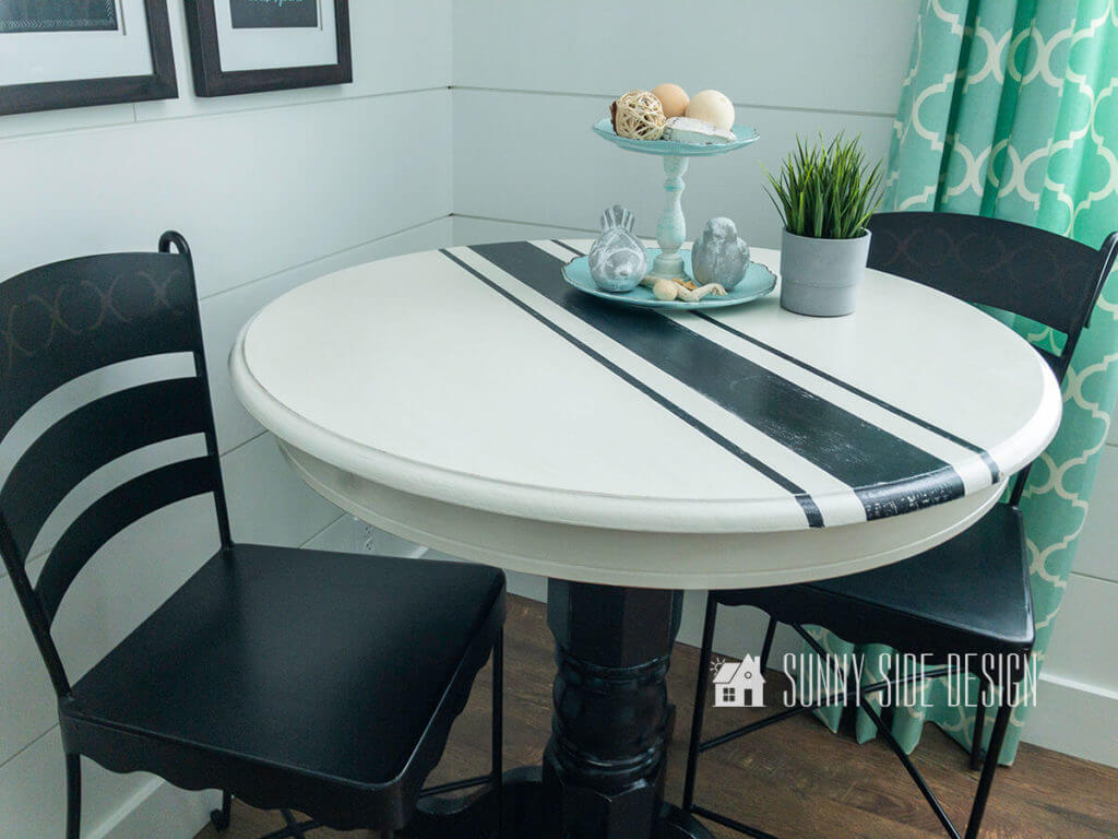 Flea market flip ideas, oak pub table is transformed with white and black chalk paint with a grain sack pattern, staged with 2 black bar stools, white shiplap wall with aqua blue quadrafoil curtain around window.