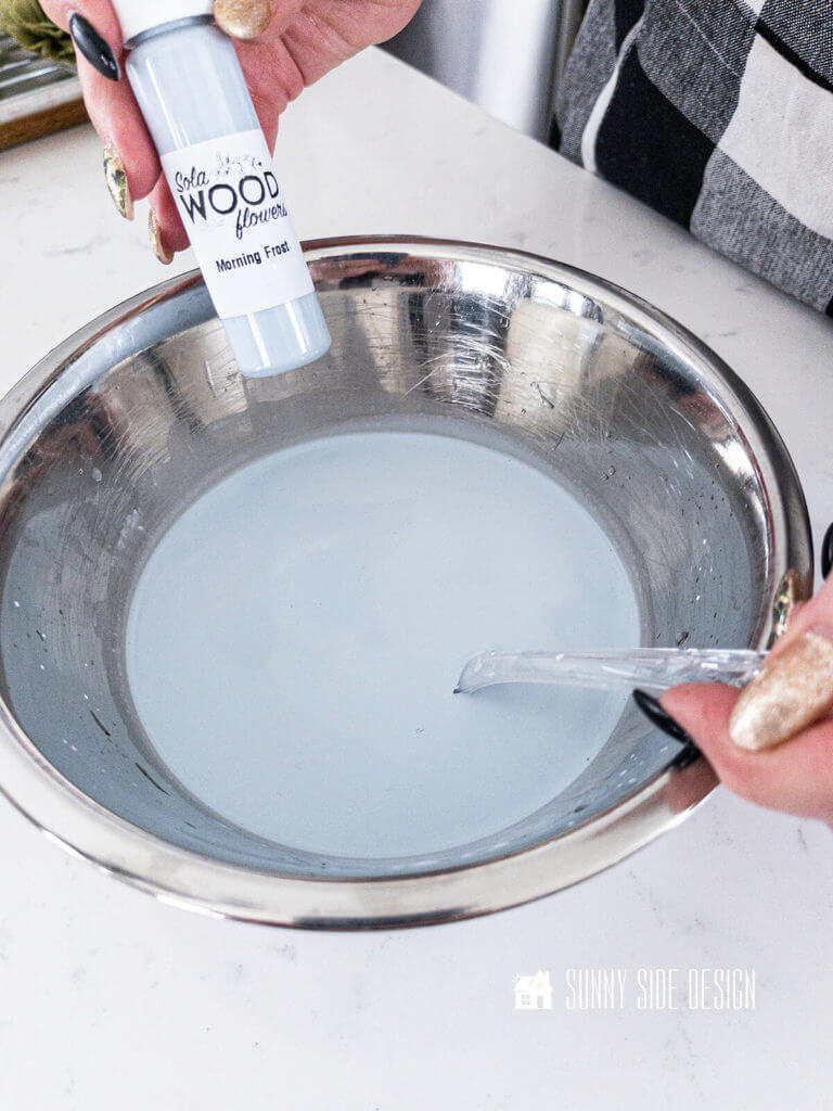 Woman's hand stirring blue dye in a stainless steel bowl.