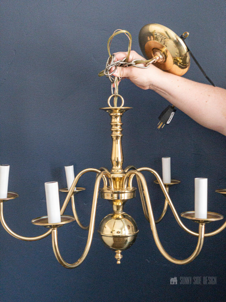 Vintage brass 6 arm chandelier against a navy blue wall before it's makeover.