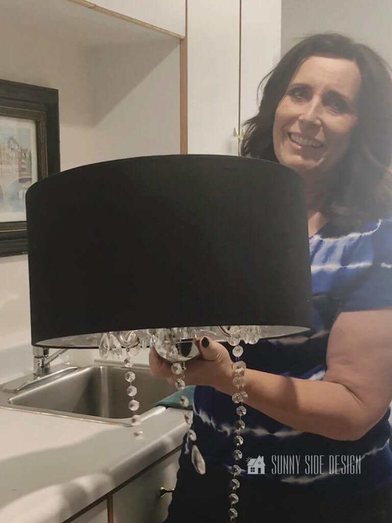 Woman holding a thrift store chandelier with broken crystals and a black lamp shade