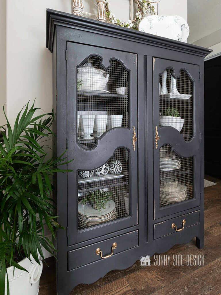 Newly black chalk painted china cabinet filed with white dishes, milk glass goblets, white vases and plants.
