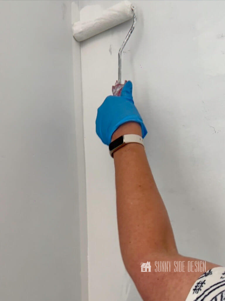 Woman's hand holding a small high density foam roller, cutting in the edges of the wall with white paint.
