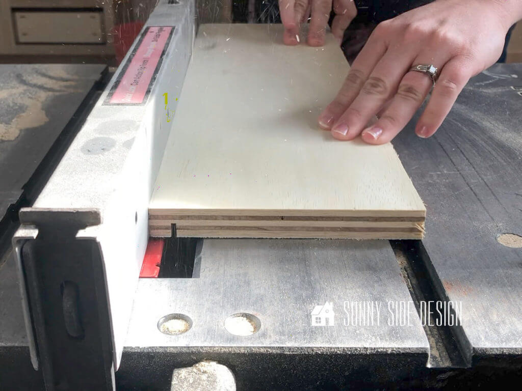 Woman's hands pushing a piece of plywood at the table saw, creating a dado groove for building a drawer box.