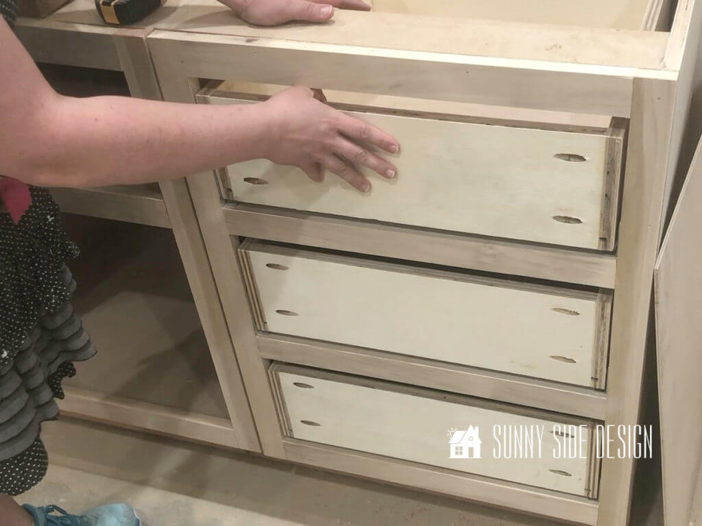 Woman's hand closing the cabinet drawer with 3 built cabinet drawers in the cabinet drawer box.