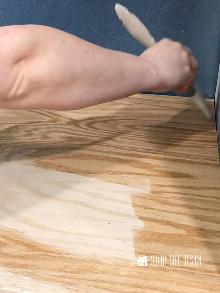 How to apply a water based stain - Woman's hand holding a paint brush, applying the water based wood conditioner before applying the stain.