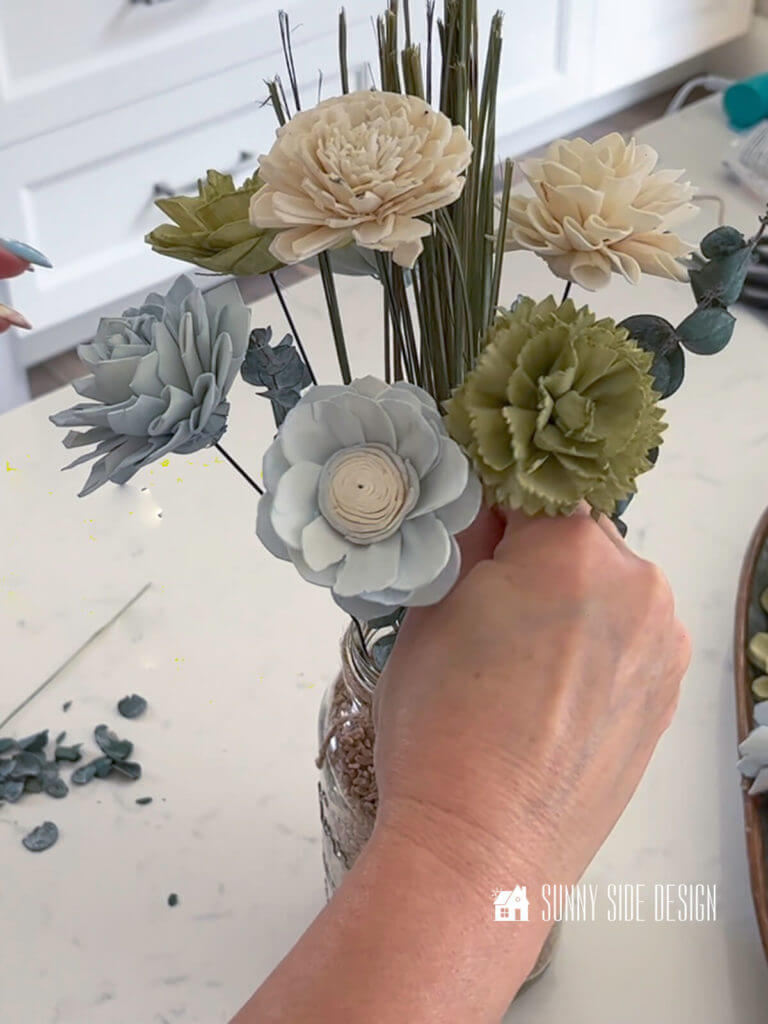 Woman's hand placing a green dyed Sola wood flower into the floral arrangement.