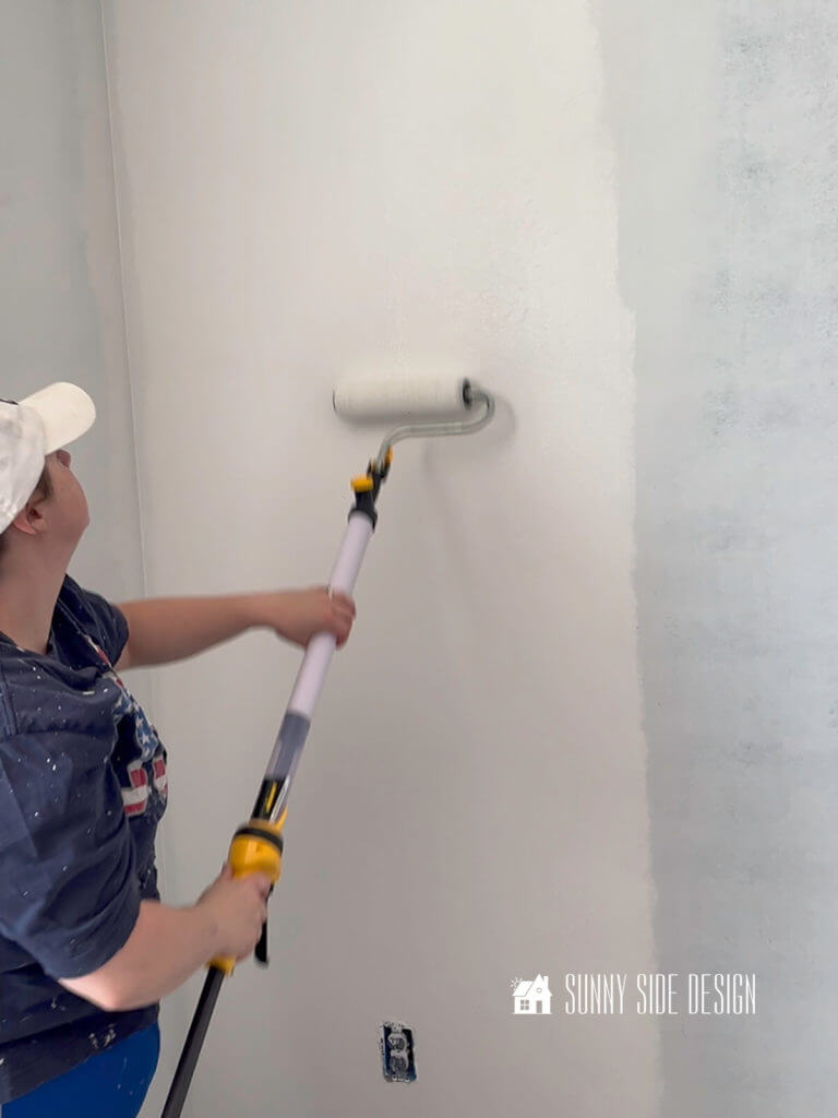 Painting a room with white paint, woman holding the Wagner paintstick EZ roller, rolling the paint on the primed wall.