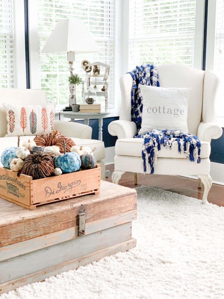 DIY Fall Decor ideas, old crate willed with various pumpkins that are natural vine pumpkins, white and blue pumpkins setting on an old trunk in a white living room.