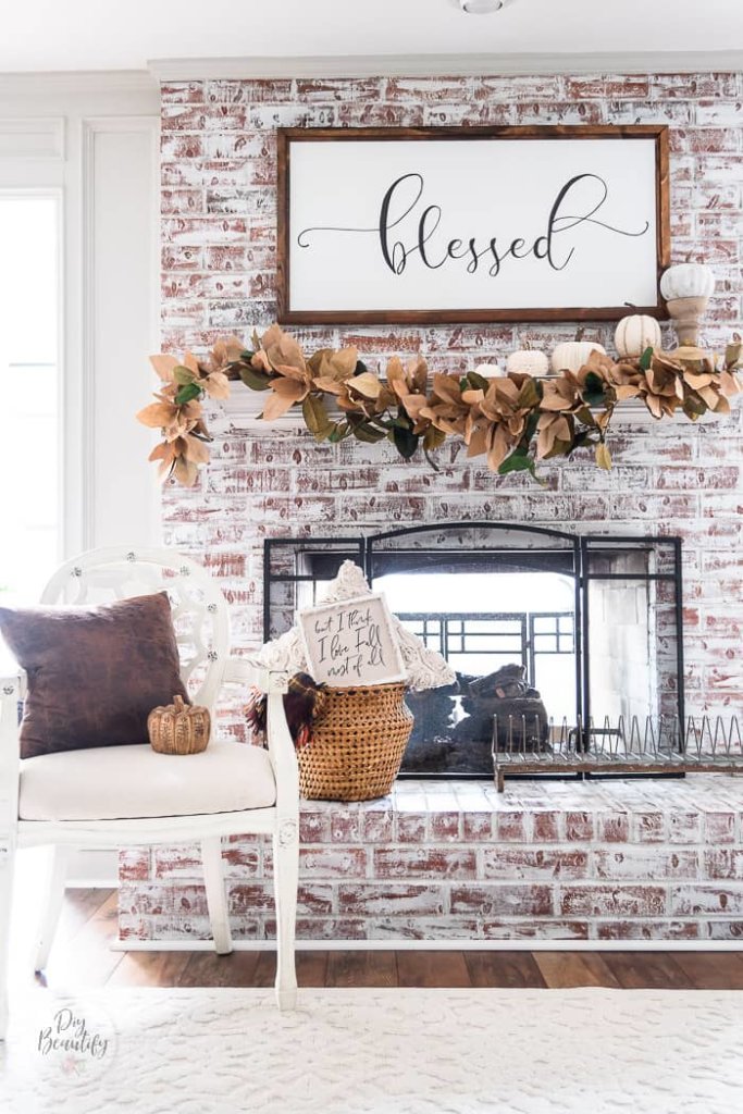 DIY Fall Decor ideas, paper bag magnolia garland across hte mantle of a German smear brick fireplace, stiled with a white chair, basket, pillows.