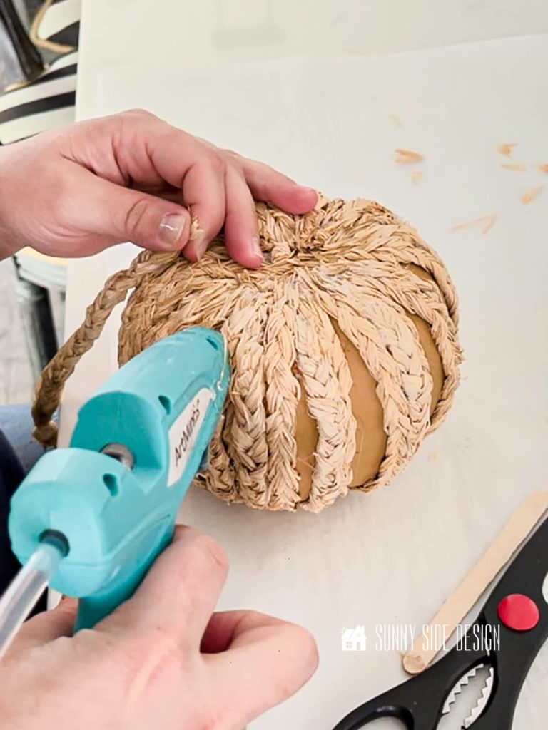 Woman applying glue to foam pumpkin to attach a piece of braided raffia.