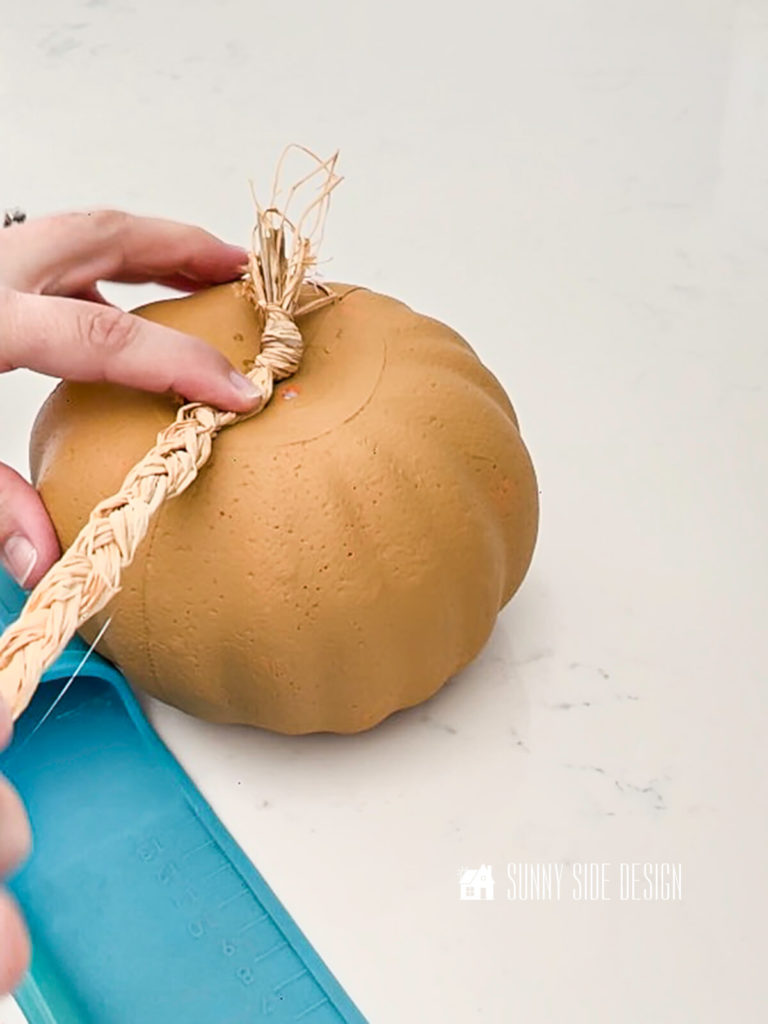 Woman's hand holding the raffia braid on the top of the pumpkin.