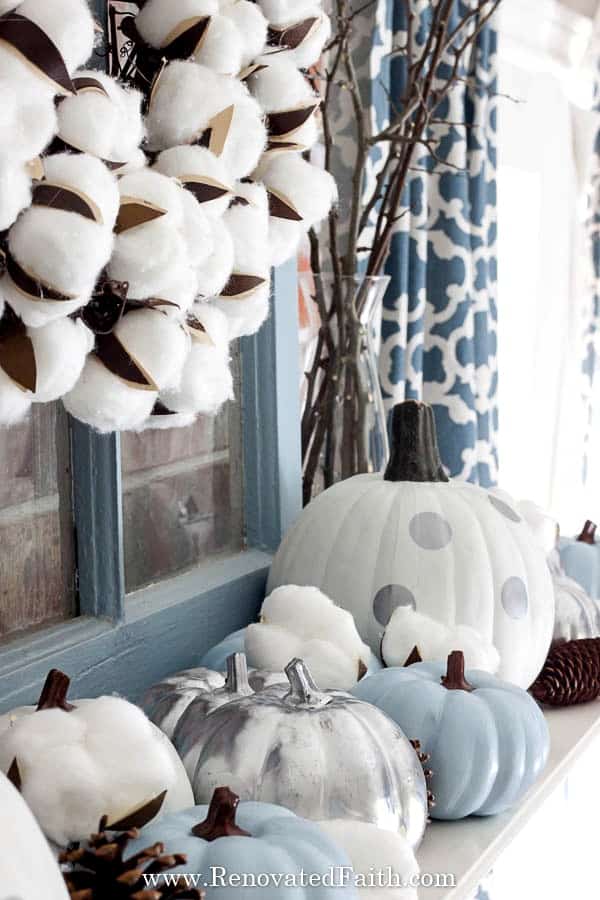 Fall mantle styled with DIY painted pumpkins in white, light blue, silver and white and silver polka dot, along with twigs in a vase and a cotton blossom wreath.