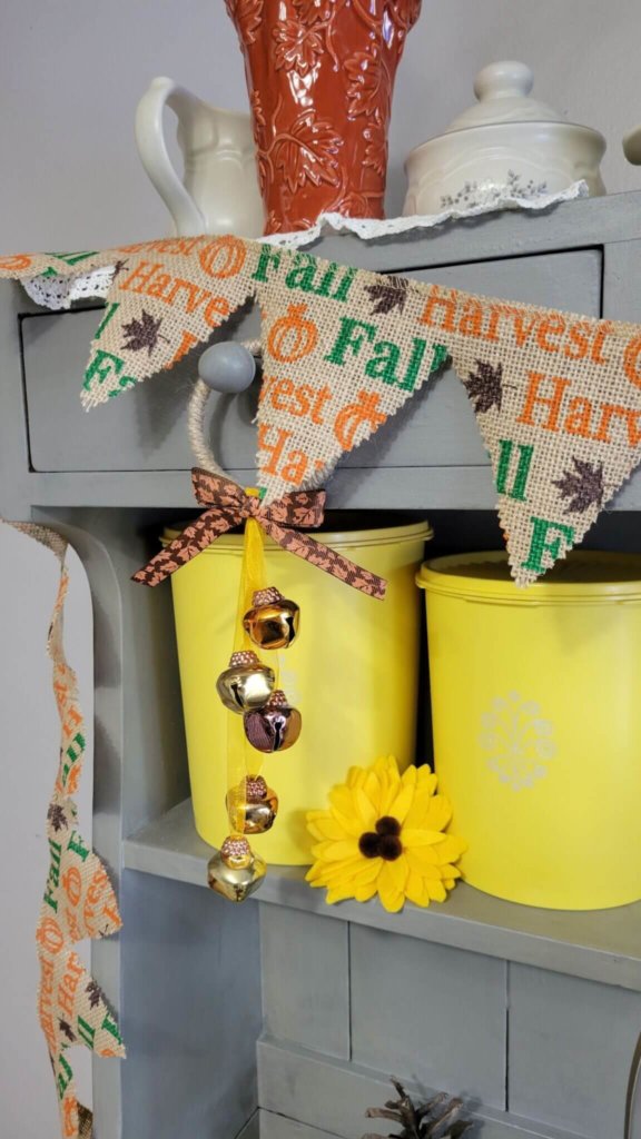 Falll burlap bunting on a grey hutch with yellow canisters and sunflowers.