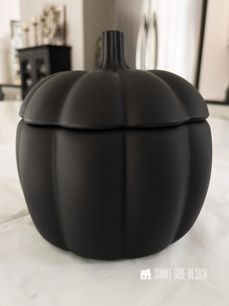 Pumpkin DIY, glass lidded pumpkin container painted with flat black spray paint setting on the kitchen counter.