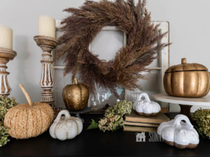 Six pumpkin DIY ideas displayed on a black cabinet with dried hydrangeas, wood candlesticks and a pampas grass wreath hung on a vintage window. Some pumpkins elevated on old books.