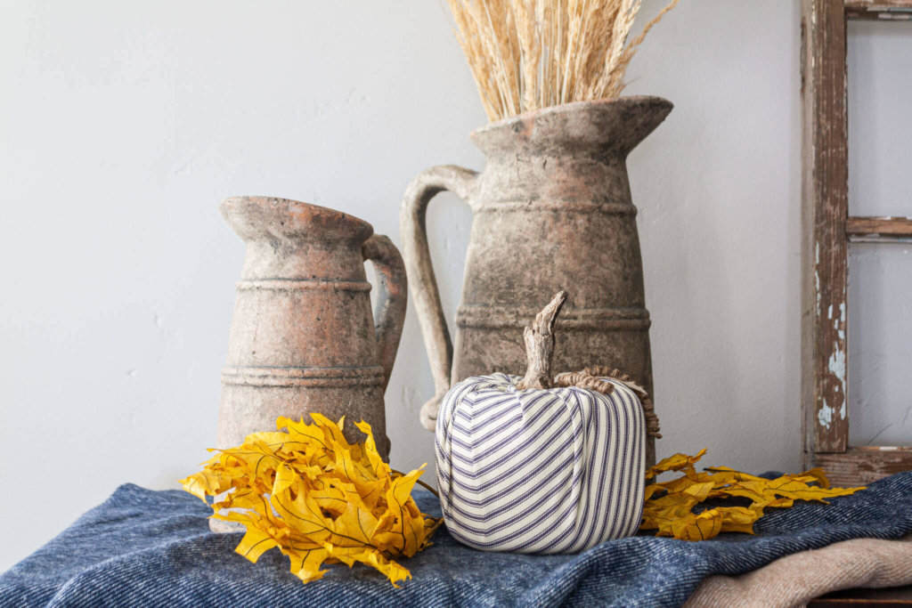 DIY Fall Decor ideas, fall grasses styled in vintage pitchers with yellow maple leaves, blue throw blanket, vintage window frame and ticking pumpkin made from a toilet paper roll.