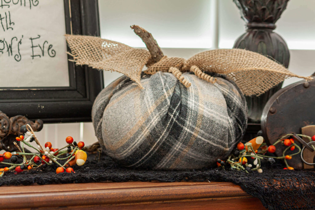 Black and grey fabric pumpkin made with a toilet paper roll, twig and burlap ribbon. Styled on a wood cabinet with bittersweet branches.