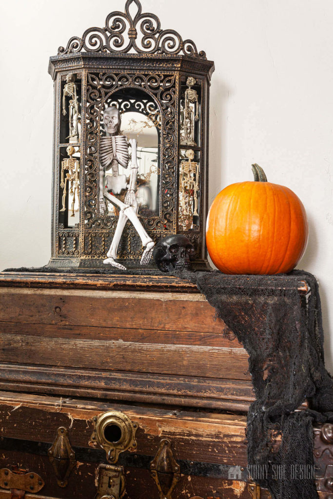 Thrift store gothic curio if filled with mini Dollar store skeletons on old trunks, black creepy cloth and an orange pumpkin.