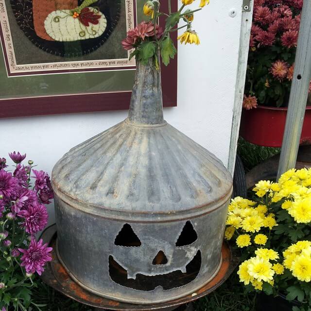 Easy Halloween decor ideas for your home. Old metal funnel is turned into a Jack-o-lantern with yellow and purple mums.
