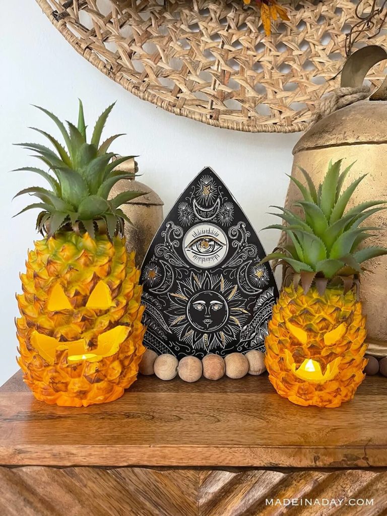 Two Playful pineapple Jack-o-lanterns with bead and basket decor on a wood table.