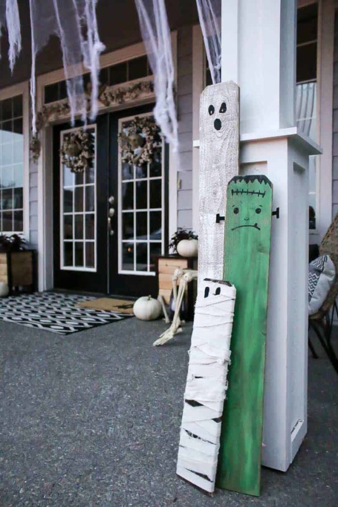 Easy Halloween decor ideas for your home. DIY porch decor from old boards, white cheese cloth draped from the porch roof, the black doors have 2 halloween wreaths.