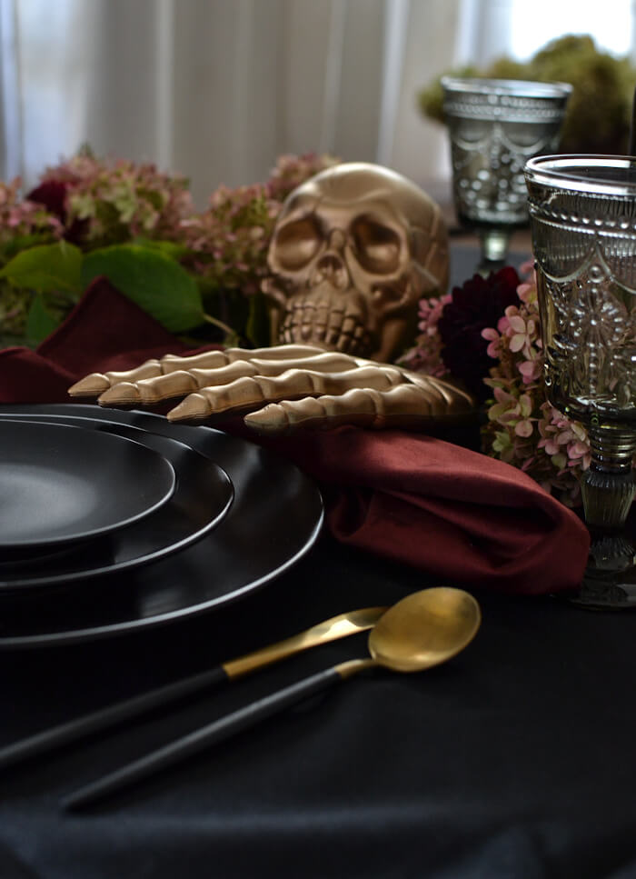 Spooky and elegane tablescape with black and gold dinnerware, dried hydrangeas and skulls and skeleton hands. easy Halloween decor ideas for your home.