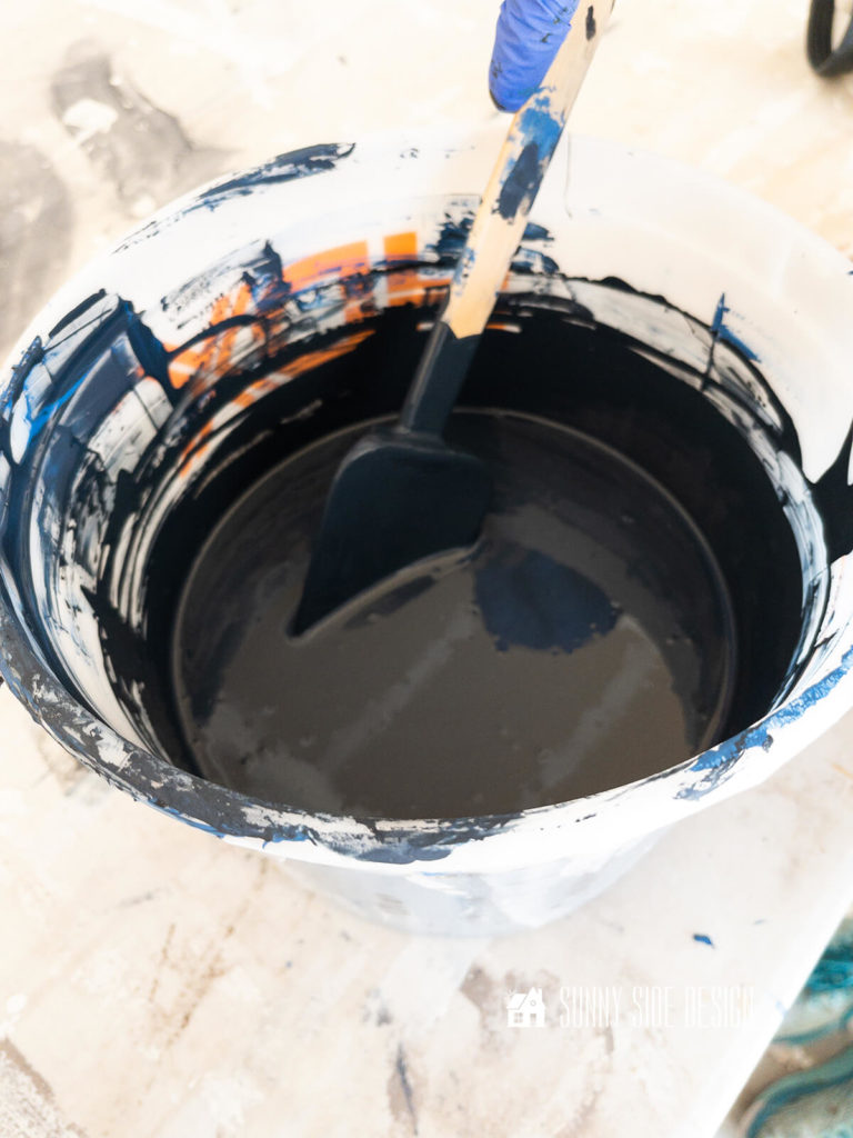 A bucket with Black Dog Salvage Furniture paint, stirring together blue ridge and black to create a navy blue