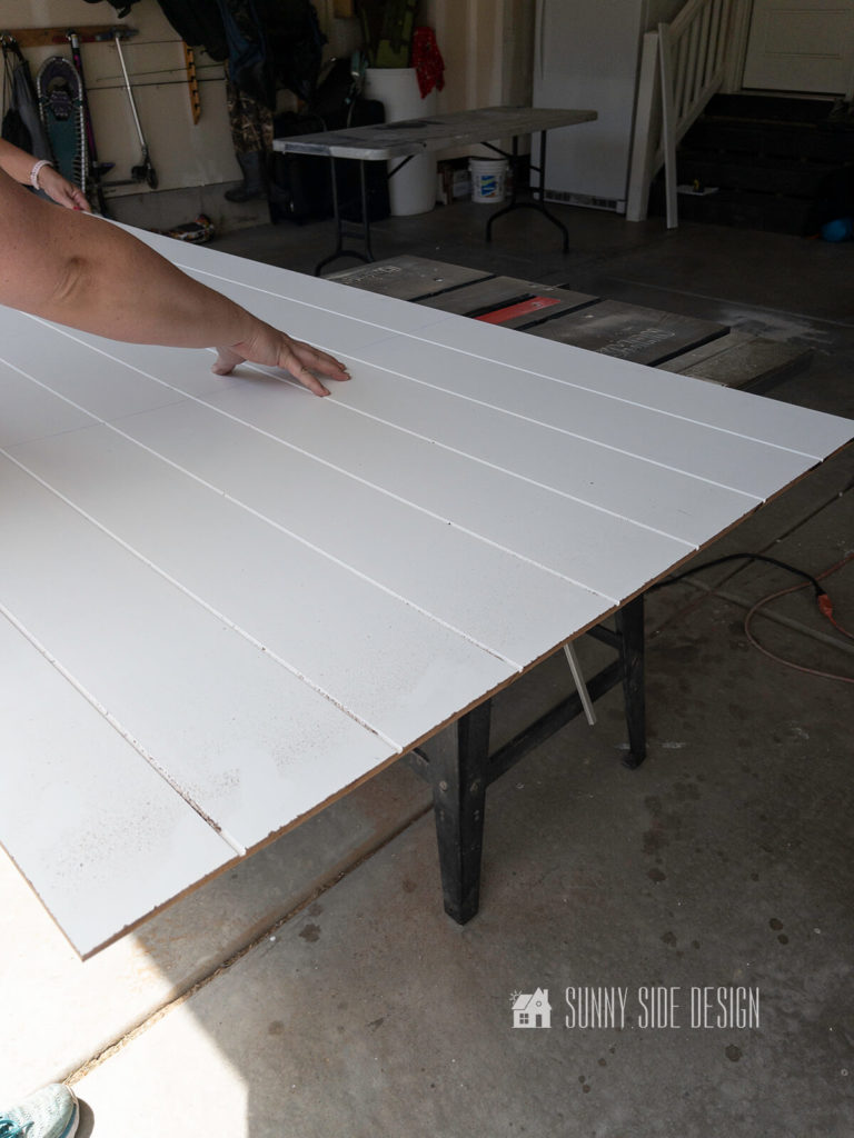 Woman guides a white primed shiplap panel through the table saw.
