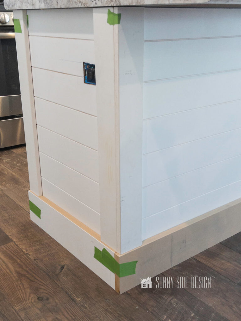 White primed trim moulding and shiplap is taped to the kitchen island shell to check for fit.
