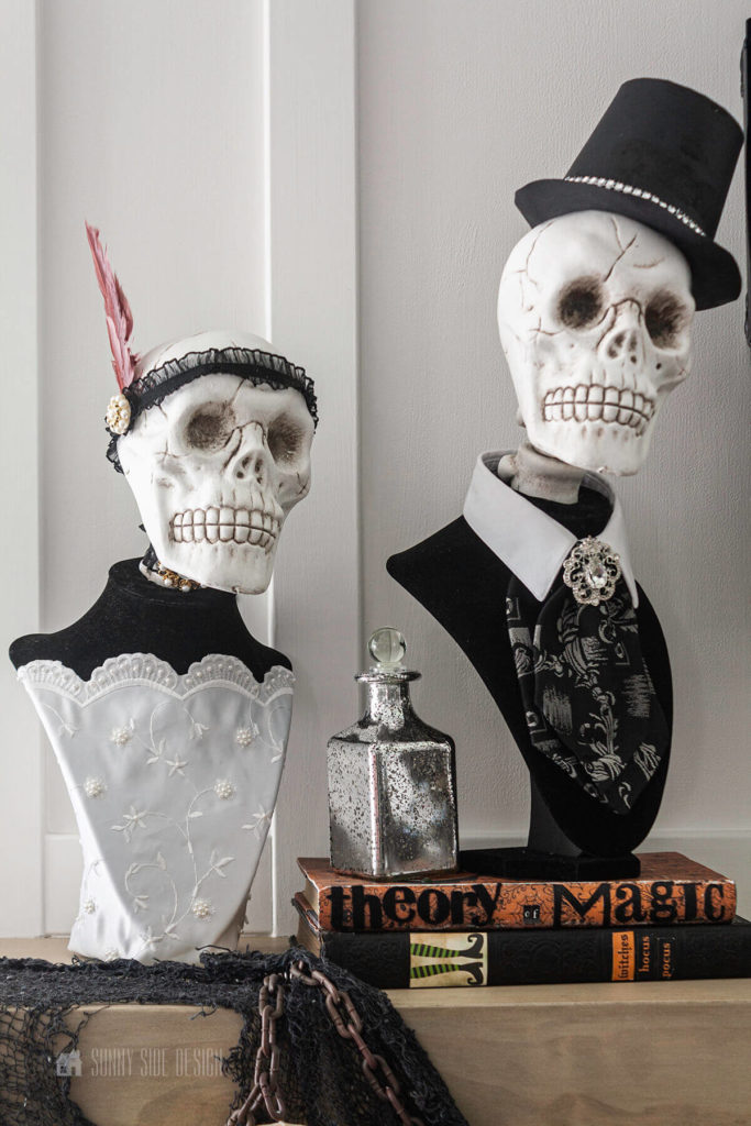DIY Black and white skull busts sit on a natural wood mantle with halloween potion books and bottle.
