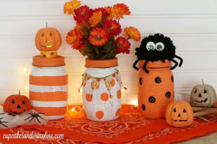 Halloween painted jars with orange and white stripes, white and orange polka dots and orange and black polka dots with mini pumpkins, spiders and orange flowers.