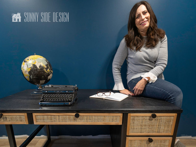 Woman sitting on the edge of the Desk makeover, black stained modern desk with rattan and oak trimmed drawer fronts with matte black drawer pulls.