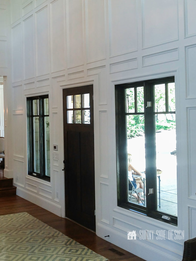 Image of picture frame moulding in a entryway enhancing windows and door. Picture frame moulding painted white with black door and window frames painted black.