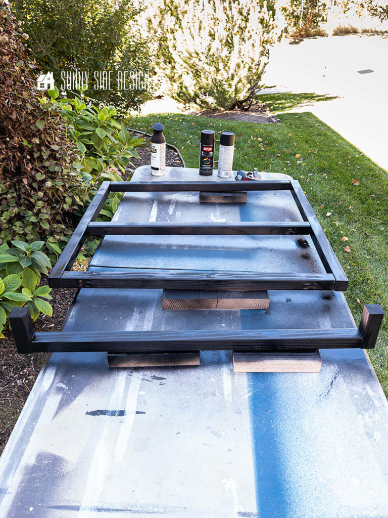 Desk makover: leg pieces for desk with black spray paint applied, setting on a table outside in the yard.