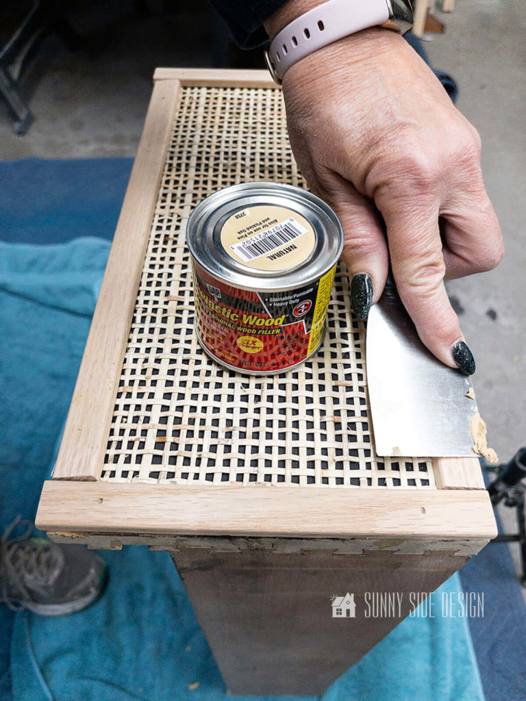 Woman applying wood putty to desk drawer front oak trim with a rattan center.