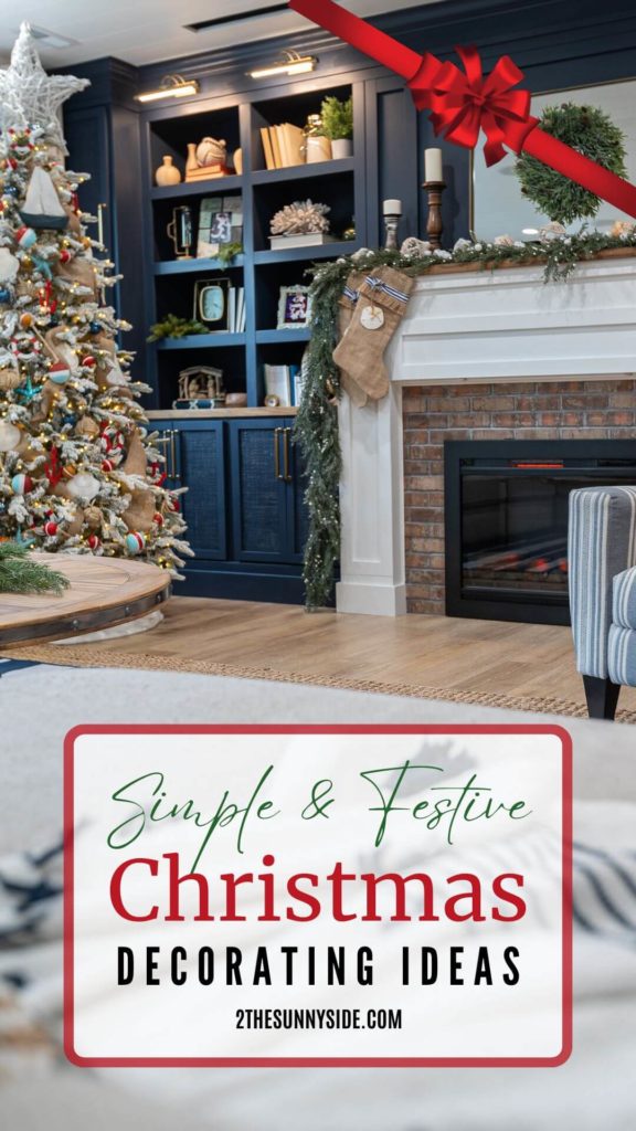 Pinterest image of decorated family room with a modern coastal Christmas tree, navy blue built in cabinets decorated with Christmas greenery, photos with Santa, nativity, realistic garland is draped along the fireplace mantle, decorated with seashells, macrame balls, candlestick and a green wreath is hung on the mirror. Burlap stockings decorated with blue and white striped ribbon, sand dollars and tiny star fish.