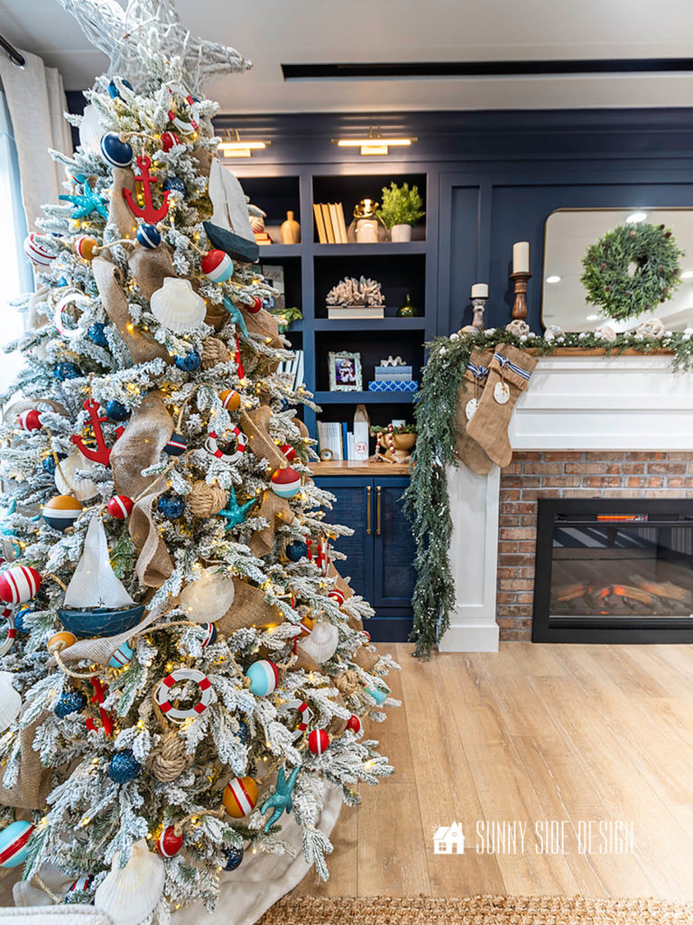 White flocked Christmas tree decorated with coastal-nautical ornaments such as; sailboats, colorful buoy garland, burlap ribbon, mini life preservers, seashells, red anchors, blue glitter starfish and navy blue ornaments.