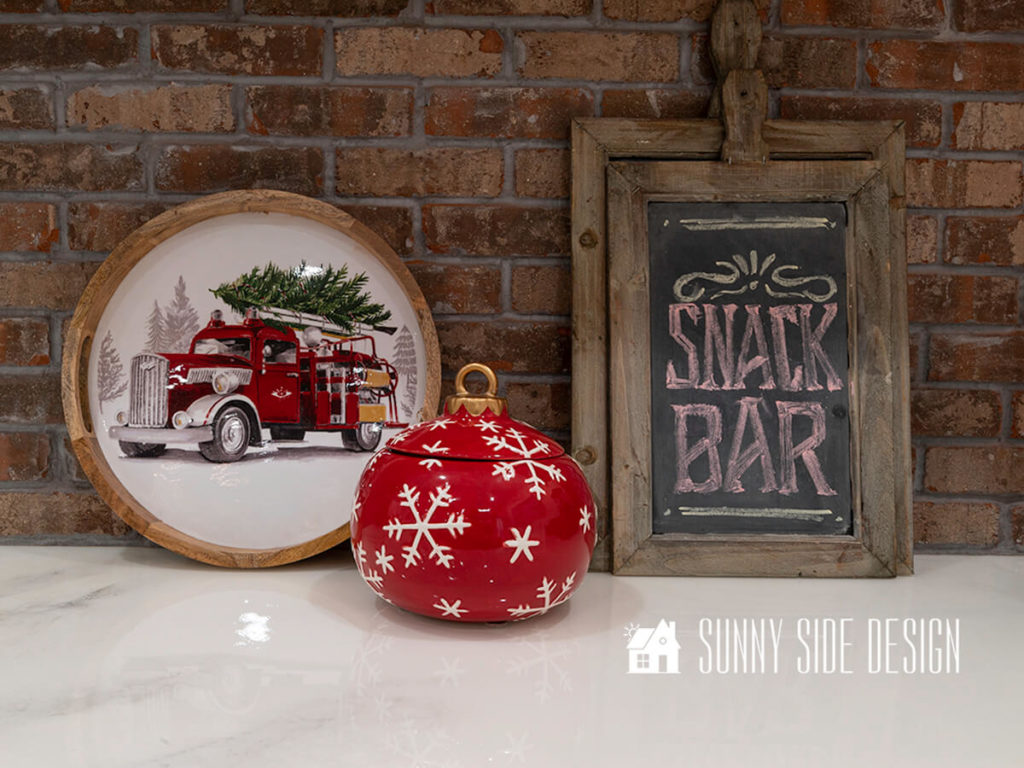 Wet bar area with marble look epoxy countertop and a rustic brick backsplash is decorated for Christmas with a festive tray and a red ornament cookie jar.