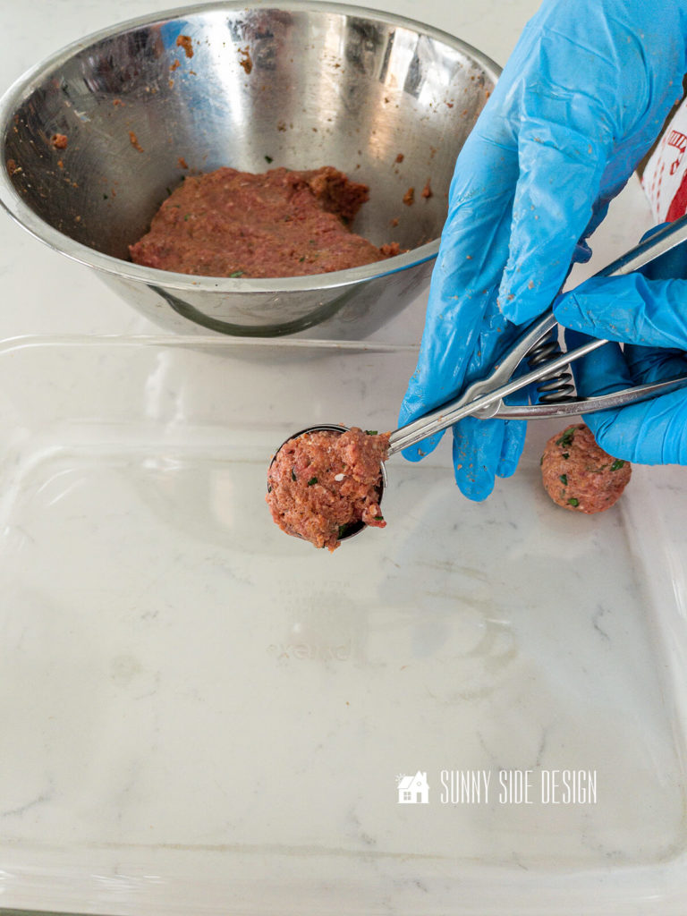 Gloved hand scoops raw meatball mixture to place in a glass pan.