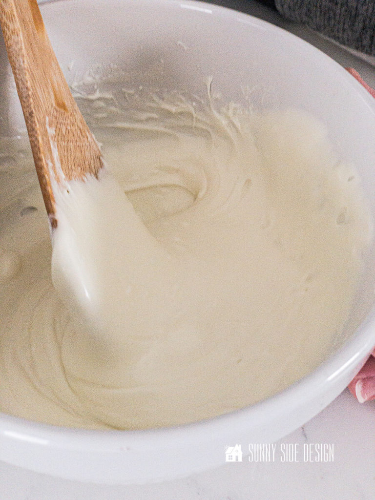 Wooden spoon stirring melted white baking chips in a white bowl.