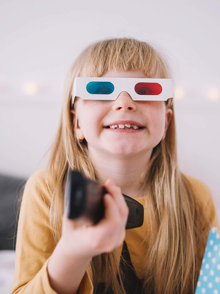 Blonde little girl wearing 3-d glasses watching movie.