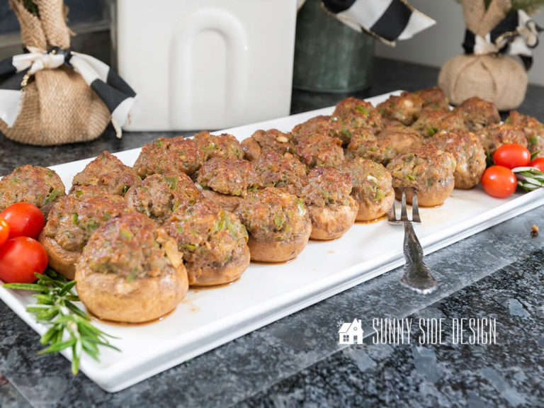 Easy stuffed mushrooms, ready to serve on a white platter and garnished with fresh rosemary and grape tomatoes.